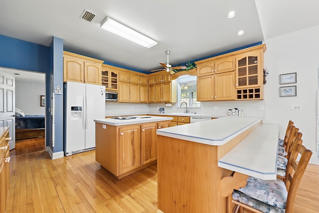 kitchen with light countertops, visible vents, light wood-style floors, white appliances, and a kitchen bar