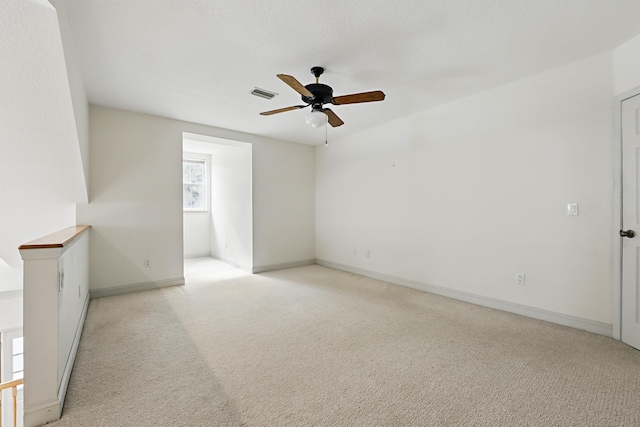 spare room featuring light colored carpet, visible vents, ceiling fan, and baseboards