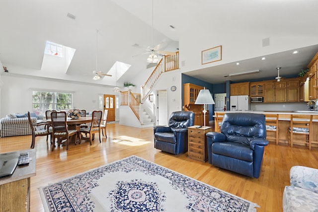 living area with light wood finished floors, ceiling fan, stairs, and a skylight