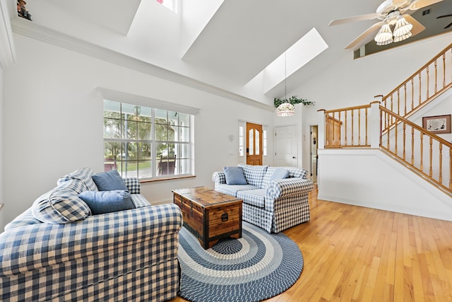 living room with a skylight, crown molding, light wood-style floors, a ceiling fan, and stairs