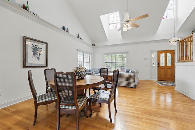 dining room featuring a skylight, baseboards, a ceiling fan, light wood-style flooring, and high vaulted ceiling