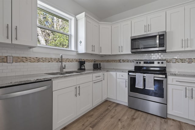 kitchen with light wood-type flooring, light stone counters, stainless steel appliances, sink, and white cabinetry