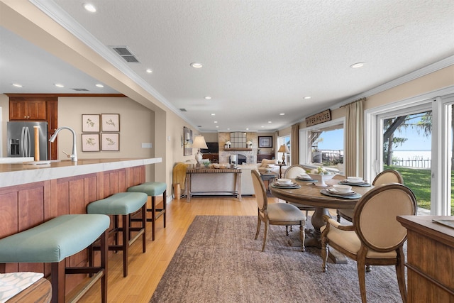 dining space featuring visible vents, light wood-style flooring, ornamental molding, and a textured ceiling