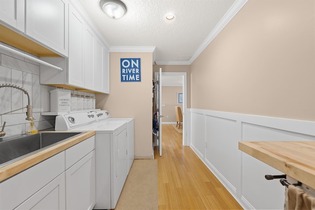 clothes washing area featuring a wainscoted wall, a sink, washing machine and clothes dryer, cabinet space, and ornamental molding