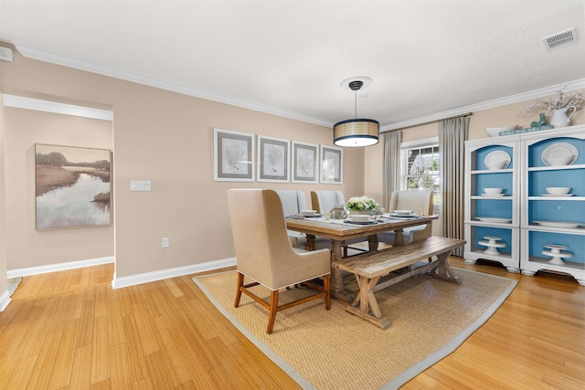 dining space featuring crown molding, baseboards, light wood-style floors, and visible vents