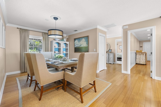 dining room with ornamental molding, baseboards, light wood finished floors, and a textured ceiling