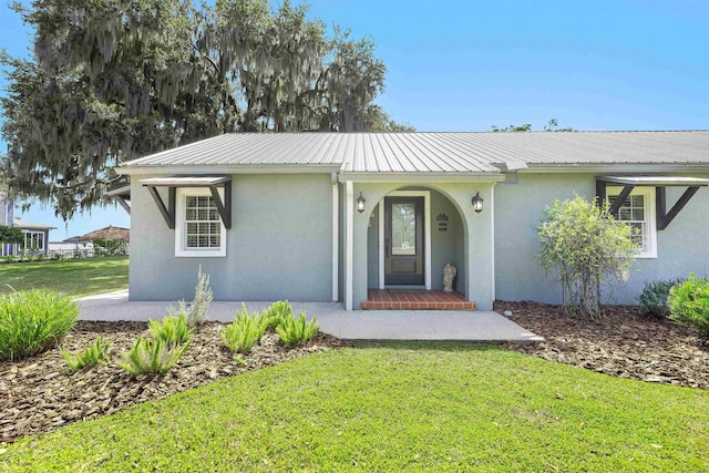 ranch-style home with a front lawn, metal roof, stucco siding, and a porch