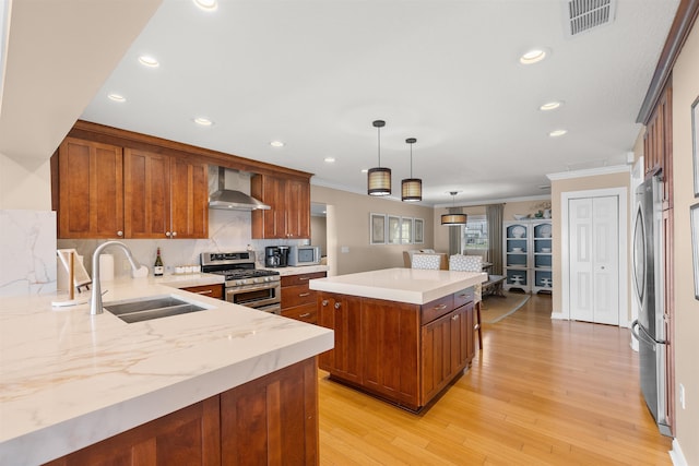 kitchen with a sink, wall chimney exhaust hood, appliances with stainless steel finishes, brown cabinetry, and visible vents