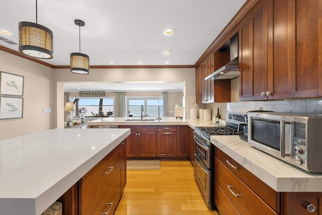 kitchen featuring light countertops, stainless steel appliances, wall chimney range hood, light wood-style floors, and ornamental molding