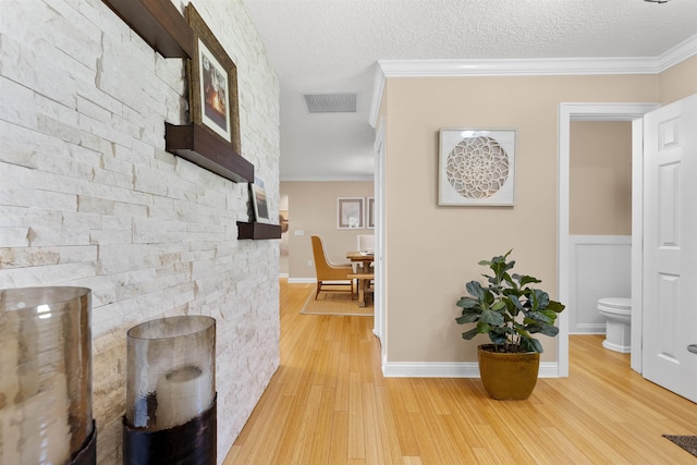 corridor featuring ornamental molding, a textured ceiling, light wood finished floors, and visible vents