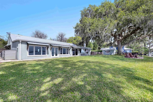 back of property with stucco siding, fence, an outdoor structure, metal roof, and a lawn