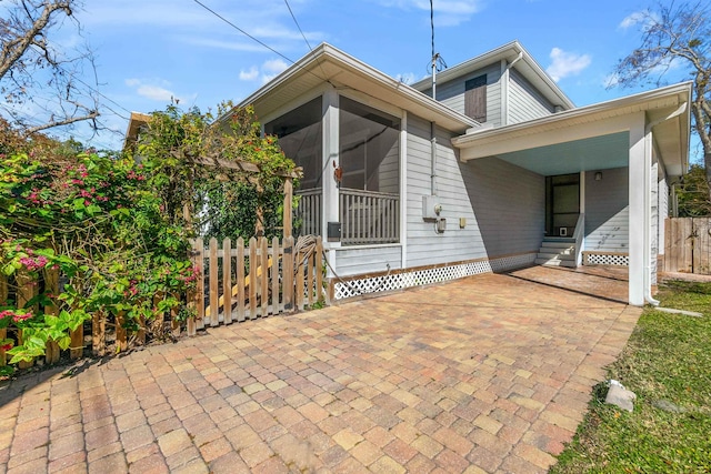 rear view of house with entry steps, a sunroom, and fence