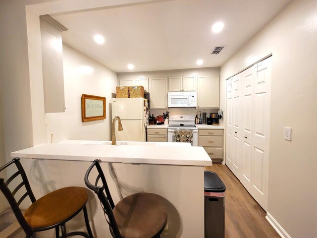 kitchen with dark hardwood / wood-style floors, white appliances, kitchen peninsula, and a breakfast bar area