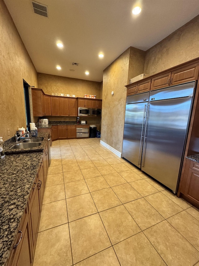 kitchen with dark stone countertops, built in appliances, sink, and light tile patterned floors