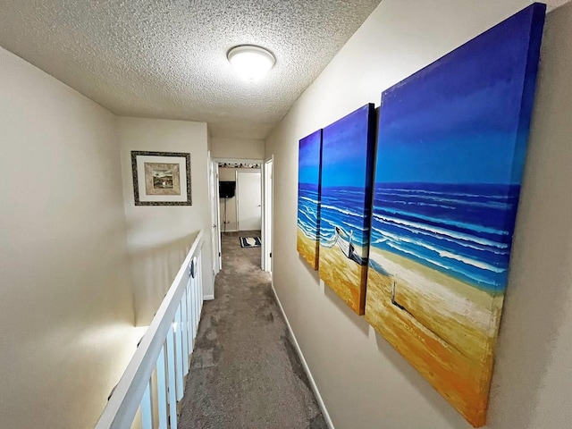 hallway with a textured ceiling, dark colored carpet, and baseboards