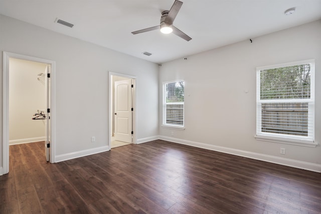 unfurnished bedroom with dark wood-style floors, a walk in closet, visible vents, and baseboards