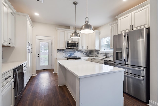 kitchen with light countertops, hanging light fixtures, appliances with stainless steel finishes, white cabinets, and a kitchen island