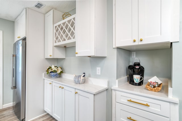 kitchen with high end refrigerator, white cabinetry, light hardwood / wood-style flooring, and a textured ceiling