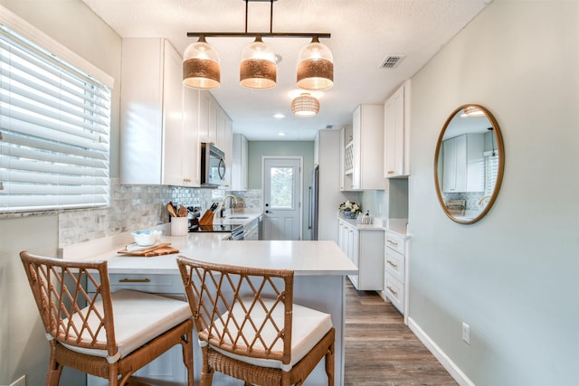 kitchen featuring kitchen peninsula, appliances with stainless steel finishes, decorative light fixtures, a kitchen bar, and white cabinetry