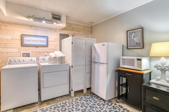 washroom with a textured ceiling, separate washer and dryer, and wooden walls