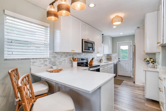 kitchen featuring kitchen peninsula, appliances with stainless steel finishes, light wood-type flooring, a kitchen breakfast bar, and white cabinets