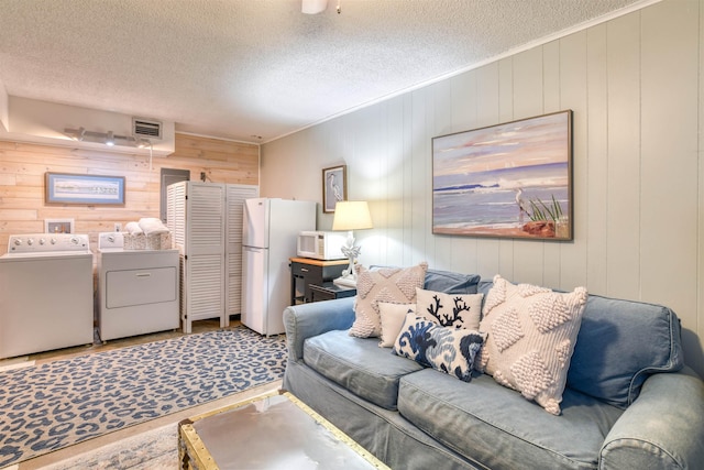 living room featuring separate washer and dryer, a textured ceiling, and wooden walls