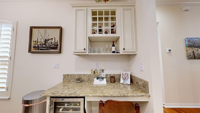 bar with beverage cooler, light wood-type flooring, and light stone countertops