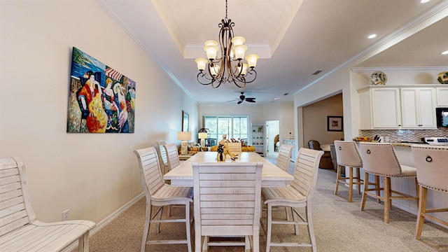 dining room with ceiling fan with notable chandelier, light colored carpet, a raised ceiling, and crown molding