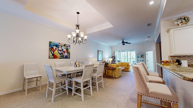 dining room featuring ceiling fan with notable chandelier, ornamental molding, light colored carpet, and a tray ceiling