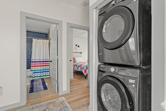 clothes washing area with baseboards, light wood finished floors, visible vents, stacked washing maching and dryer, and laundry area