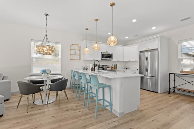 kitchen featuring a breakfast bar area, stainless steel appliances, visible vents, a peninsula, and light countertops