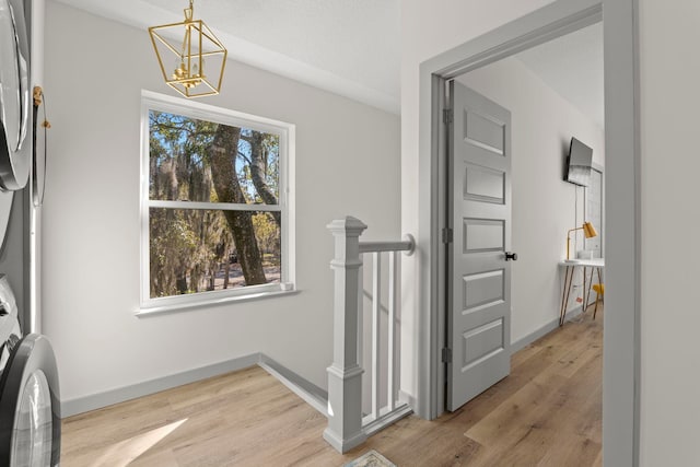 interior space with baseboards, a notable chandelier, light wood-style floors, and an upstairs landing
