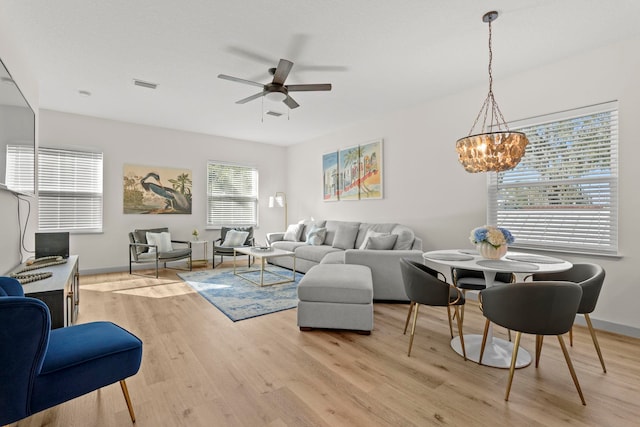 living room with baseboards, visible vents, light wood-style flooring, and ceiling fan with notable chandelier