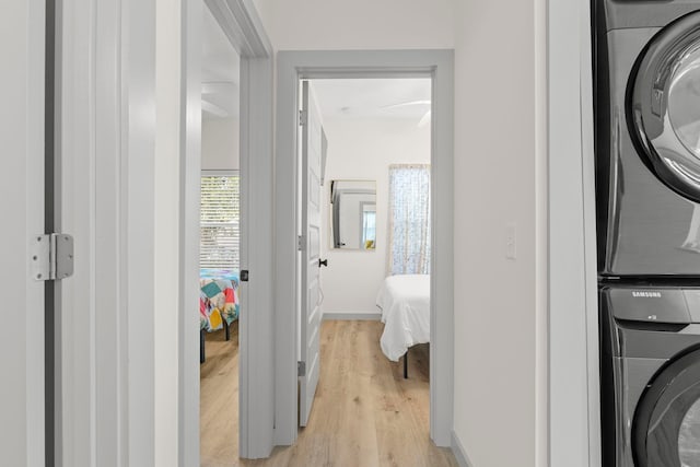 washroom with baseboards, light wood finished floors, stacked washing maching and dryer, and laundry area