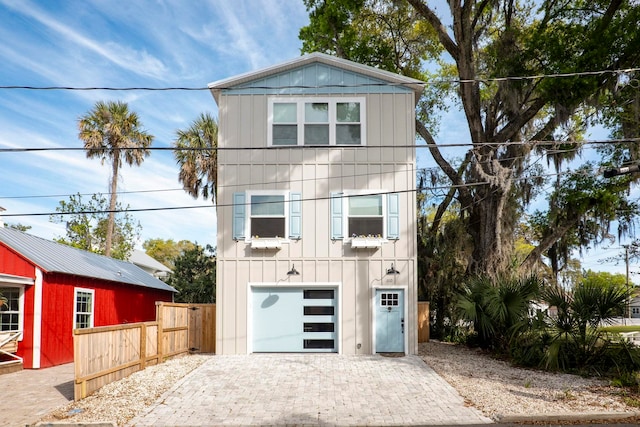 view of front facade with board and batten siding, decorative driveway, fence, and a garage
