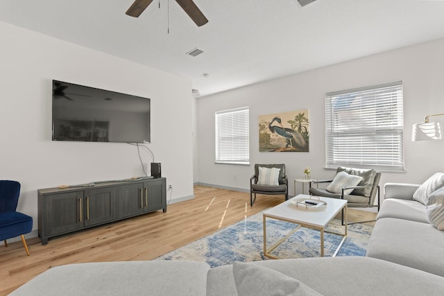 living area featuring baseboards, light wood-style floors, visible vents, and ceiling fan