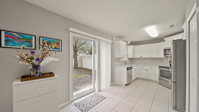 kitchen with sink, light tile patterned floors, appliances with stainless steel finishes, white cabinetry, and decorative backsplash