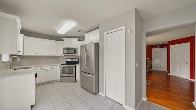 kitchen featuring tasteful backsplash, sink, white cabinets, light tile patterned floors, and stainless steel appliances