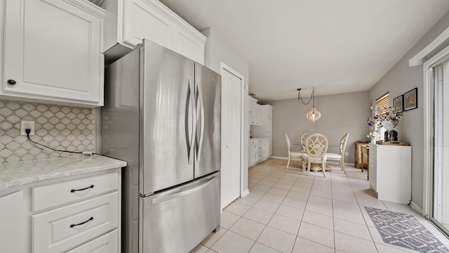 kitchen with light tile patterned floors, stainless steel refrigerator, white cabinetry, backsplash, and light stone countertops