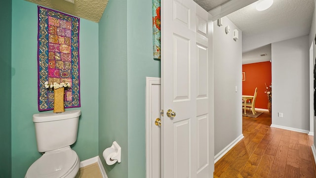 bathroom with wood-type flooring, toilet, and a textured ceiling