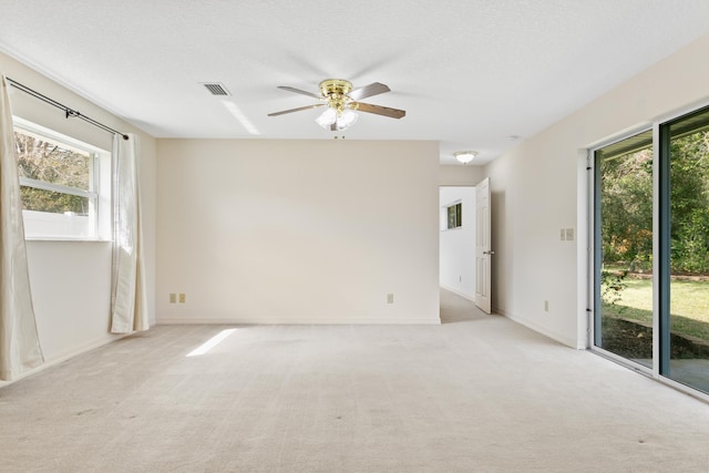 empty room with light carpet, baseboards, visible vents, ceiling fan, and a textured ceiling