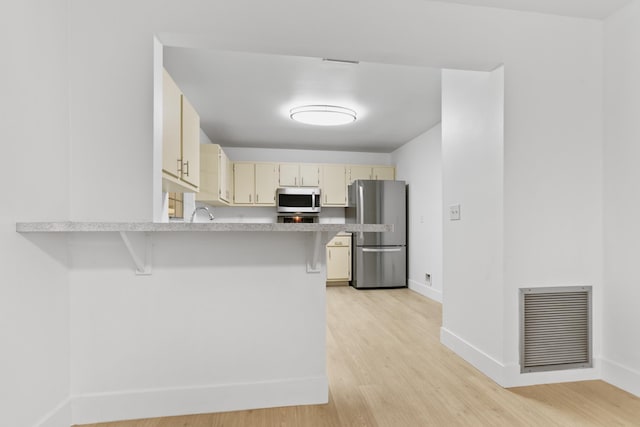 kitchen featuring cream cabinetry, stainless steel appliances, light countertops, visible vents, and a peninsula