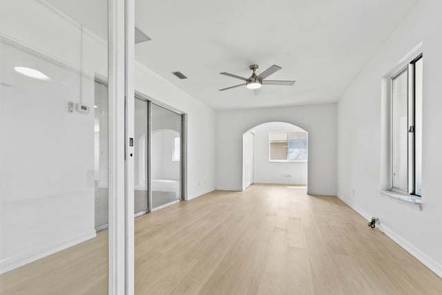 unfurnished room featuring baseboards, visible vents, arched walkways, a ceiling fan, and light wood-style flooring