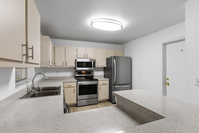 kitchen featuring light wood finished floors, appliances with stainless steel finishes, cream cabinets, light countertops, and a sink