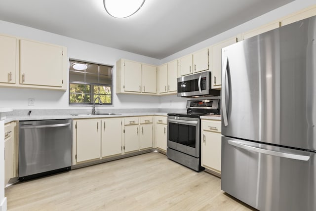 kitchen featuring appliances with stainless steel finishes, light countertops, a sink, and cream cabinets