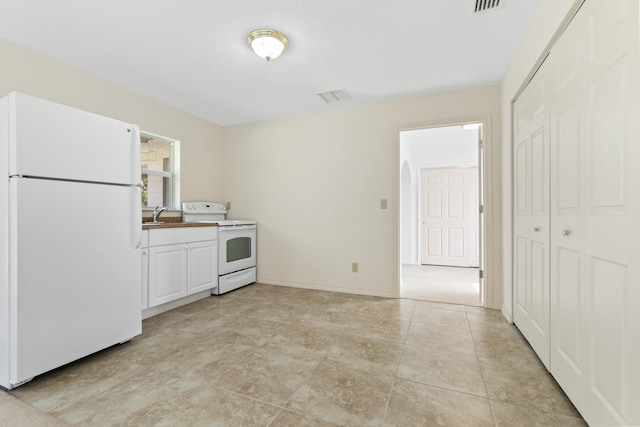 kitchen with white appliances, a sink, visible vents, white cabinetry, and baseboards