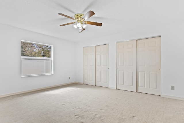 unfurnished bedroom with baseboards, carpet floors, ceiling fan, and multiple closets