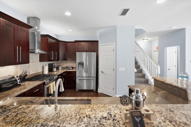 kitchen with sink, backsplash, stainless steel appliances, light stone counters, and wall chimney exhaust hood