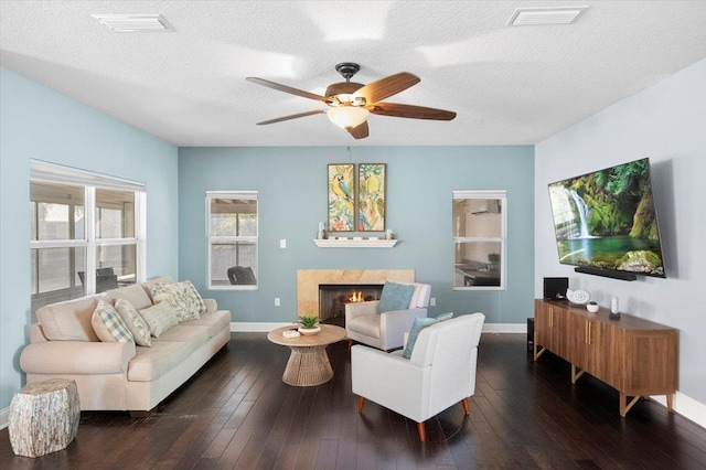 living room with dark hardwood / wood-style flooring, ceiling fan, a premium fireplace, and a textured ceiling