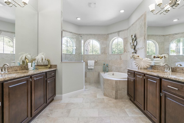 bathroom featuring vanity, a relaxing tiled tub, and an inviting chandelier